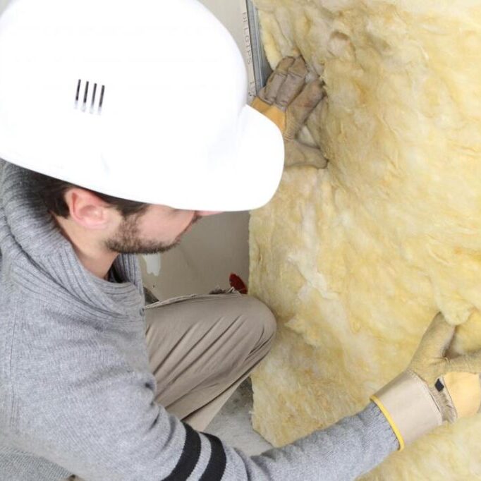 man in hard hat tacking fiberglass batt to a wall Tacking fiberglass batt to a wall